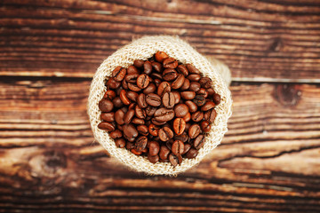 Coffee beans in a burlap bag on a wooden background.