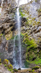 A high waterfall hidden between the high mountain sides in Schiefling am See, Austria. Water falls freely until the very bottom. Sides of the rocks are overgrown with moss. Hidden gem.