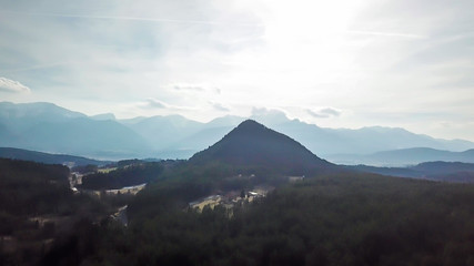 Naklejka na ściany i meble Areal, drone view on Kathreinkogel in Schiefling am See, Austria. The hill has a perfect pyramid shape. It is overgrown with forest. There are high Alps in the back. Little village under the hill.