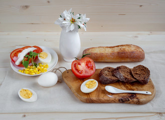 Prepare hearty breakfast of fresh bread, boiled eggs, tomato and corn salad with mayonnaise.