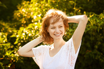 Naklejka na ściany i meble Portrait of happy pretty young woman in park at sunny summer day