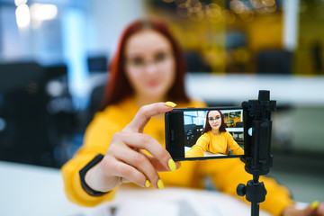 Hand woman holding camera for recording video while sitting at office. Teenager student in a yellow...