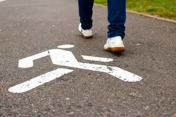 White pedestrian sign on sidewalk and feet of woman pedestrian