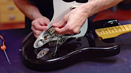 Luthier fixing electrical components of a guitar - obrazy, fototapety, plakaty