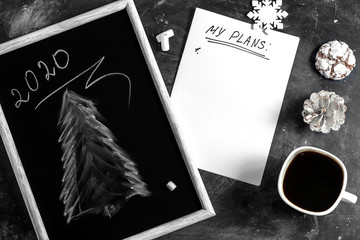 Winter Christmas composition. A cup of coffee on a table with a white sheet of paper and a black slate board with a drawing of a Christmas tree. Christmas mood concept. Top view, flat lay