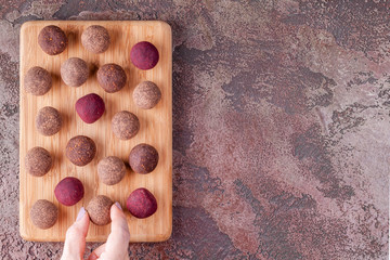 Woman Hand Take a Homemade Raw Vegan Cacao Energy Balls from Wooden Board on Marble Background. Healthy Sweets from Nuts and Dates. Concept of Natural Vegetarian Handmade Dessert. Top View. Copy Space