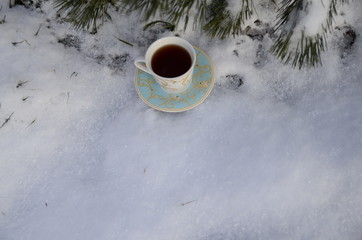 Obraz na płótnie Canvas Winter. December. Against the backdrop of evergreens covered with white fluffy snow, there is a cup of freshly brewed fragrant black tea.