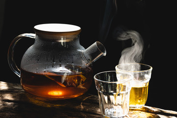 The steam from a cup or pot of coffee or tea on the old wood table and black background, Warm...