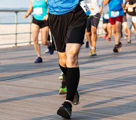 Runners legs with compression socks racing on boardwalk by the beach