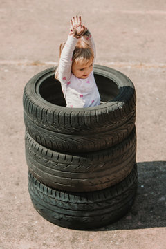 From above of happy adorable little girl standing in stack of car tires while having fun and playing outdoors on summer day