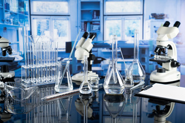 Science laboratory. Beakers, test-tubes and microscope on glass table in the laboratory.