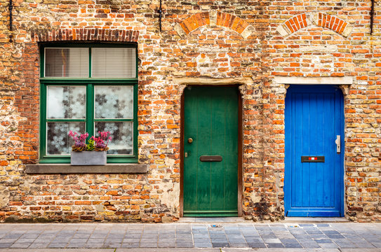 The facade of an old brick house with a window and two wooden doors