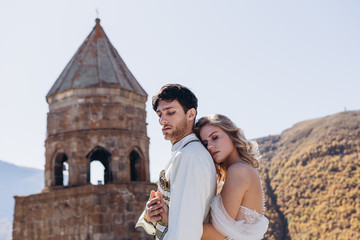 Georgian couple of brides are photographed against the backdrop of a wedding church at the top of a mountain