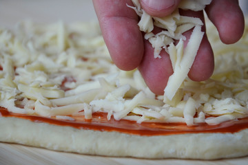 A man's hand lays out cheese on a dough, with tomato sauce and slices of sausage. Concept: cooking Italian pizza with mozzarella.