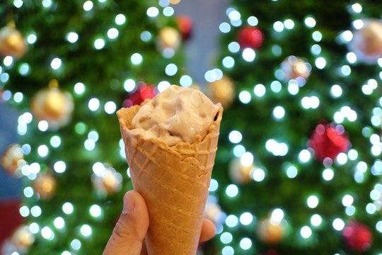  A female hand holding a soft cone of vanilla ice cream with blur a Christmas tree and beautiful bokeh light at night