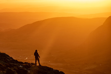 Obraz premium A hiker silhouetted against beautiful orange sunrise in mountains