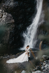 noise effect, selective focus: wedding couple model shoot, attractive bride in an incredibly beautiful long-flowing dress and groom in a waterfall background