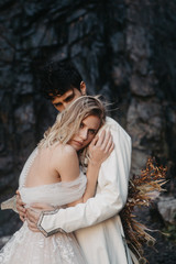 noise effect, selective focus: incredibly enamored brides hugging, kissing and posing for a photo on the incredible rocky mountains background with a big waterfall