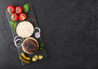 Fresh grilled minced pepper beef burgers on stone chopping board with buns onion and tomatoes on black background. Salty pickles and basil