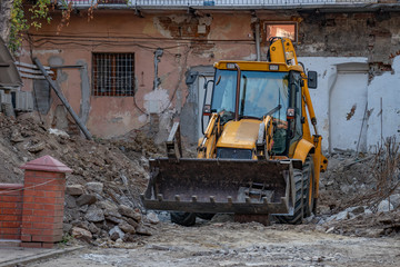 Fototapeta na wymiar A large yellow excavator stands among the ruins of an old house