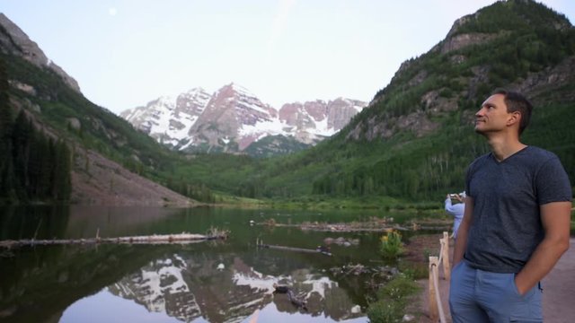 Maroon Bells lake at sunrise with tourist man standing in Aspen, Colorado during blue hour dawn with rocky mountain peak and snow