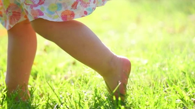 Adorable little one year old Baby Girl making her first steps outdoor. Slow Motion Video Footage of the First Steps of the Kid. Sunny day and Green Grass. Slow motion 4K UHD video