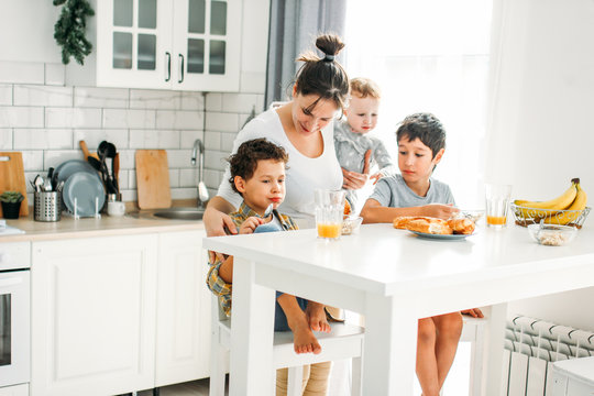 Young woman mom with baby girl on hands cooking breakfast on bright kitchen at home, large happy family