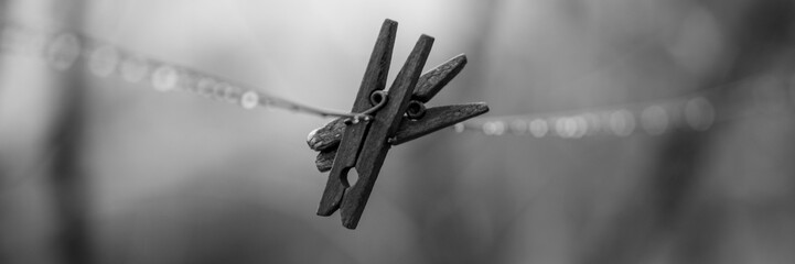 Two old wooden clothespins hanging on a clothesline in rainy weather, bw photo.