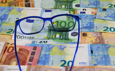 Symbol for clear view on financial market, prediction of price trend:  Eyeglasses on pile of Euro paper bank notes enlarge 100 euro bill