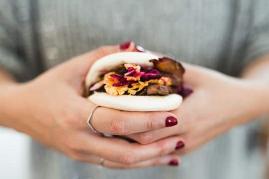 From above of crop hands of woman holding traditional Asian sandwich steamed bun with meat and vegetables