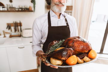 Happy mature man wearing apron bringing roasted turkey