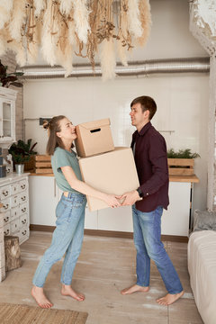 Side view of young couple making effort and carrying cardboard boxes with stuff in house