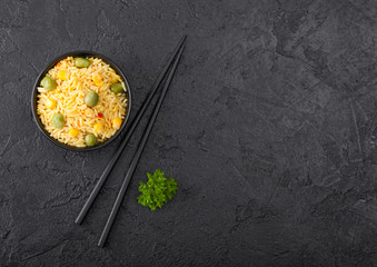 Black bowl with boiled organic basmati vegetable rice with black chopsticks on black stone background. Yellow corn and green peas with paprika slices. Space for text
