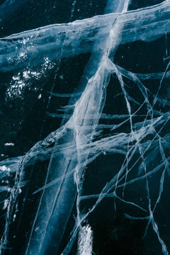 Closeup of dark natural ice texture with large cracks on frozen Siberian river on wintertime 