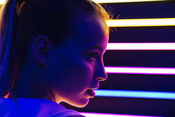 Image of young woman standing by multicolored neon illumination indoors