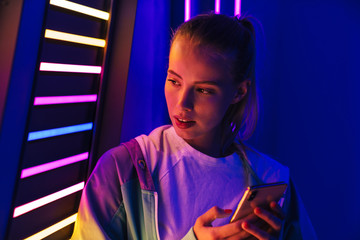 Image of woman holding smartphone by multicolored neon illumination indoors © Drobot Dean