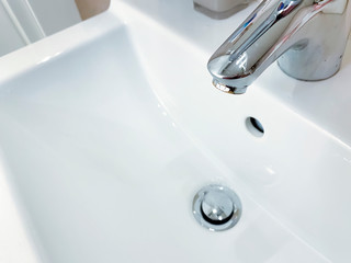 Chromed faucet with lever to mix hot and cold water on a modern white sink in a bathroom