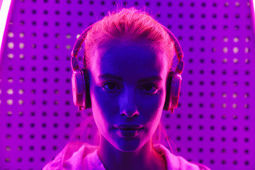 Image of woman listening to music with headphones over neon illumination