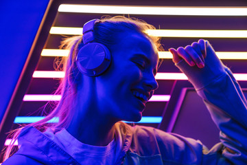 Image of woman listening to music with headphones over neon illumination