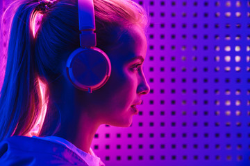 Image of woman listening to music with headphones over neon illumination
