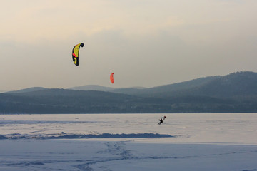snowkiting extreme winter sport. athletes on a wild winter mountain lake in the evening at sunset ride. fresh white snow and wind.