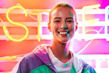 Image closeup of young woman standing over multicolored neon text sign
