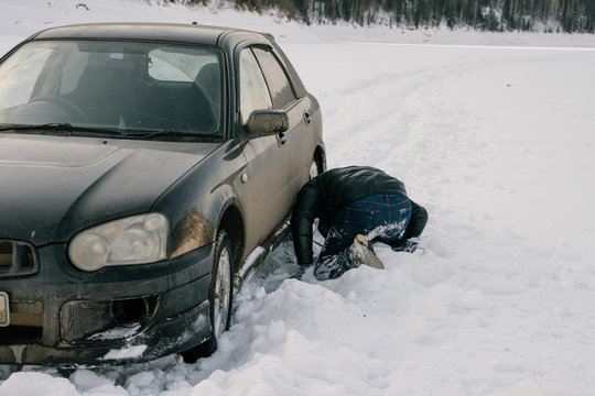 Back view of man having problem with car and changing wheel on empty snowy road during road trip in Siberian countryside 