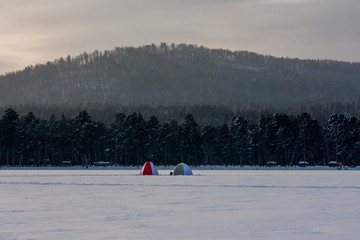 tents for winter fishing on a huge mountain lake. winter landscape. pure white snow. Fishermen catch fish in the fresh air. people's hobbies and sports