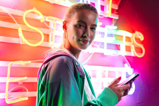 Image of beautiful woman holding smartphone over neon text sign