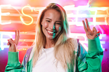 Image of woman showing peace fingers over multicolored neon text sign