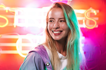 Image closeup of blonde woman smiling over multicolored neon text sign