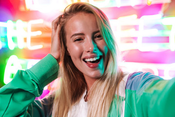 Image closeup of blonde woman smiling over multicolored neon text sign