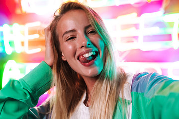 Image closeup of blonde woman smiling over multicolored neon text sign