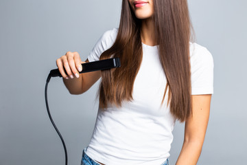 Young woman doing hairstyle with hair straightener isolated on gray background